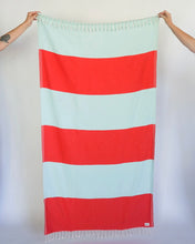 Load image into Gallery viewer, the State the Label Lattice Turkish Towel in Sunrise being held up in front of a neutral background by two hands entering the corners of the frame