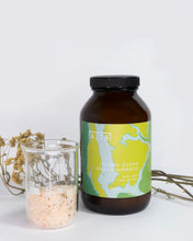 Load image into Gallery viewer, ALTR Bath Salts in Inland Ocean package sitting beside a beaker full of bath salts in front of a dried flower stem