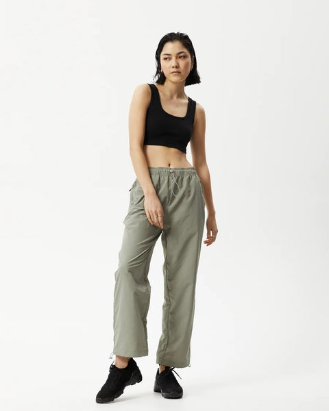 Afends Women's Octave Spray Pant in Olive on a model posing with one knee bent and her eyes toward her right shoulder
