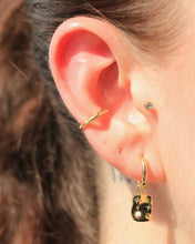 Load image into Gallery viewer, the the Horace Hammered Ear Cuff in gold stacked on an ear with a stud and dangly earring
