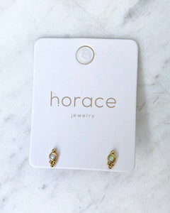 the Horace Gemma Stud Earring in gold on a branded card laying on a marble surface