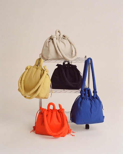 five Ölend Ona Soft Bags in multiple colours sitting on, hanging on and sitting in front of a wire rack all on a neutral background