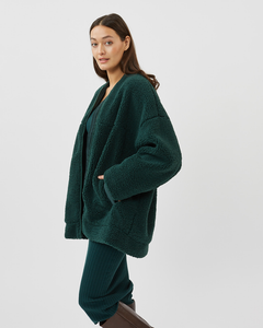 Side view of a model with her hand in her pocket wearing the Minimum Women's Bavory Jacket in Pine Grove over a green dress