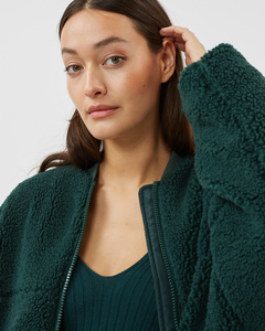 close up view of a model tucking her hair behind her ear wearing the Minimum Women's Bavory Jacket in Pine Grove open over a green v neck