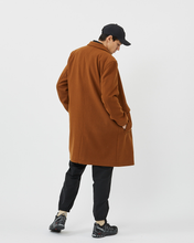 Load image into Gallery viewer, Back view of the Minimum Men's Balano Coat in Monks Robe worn on a model with black pants and a black cap