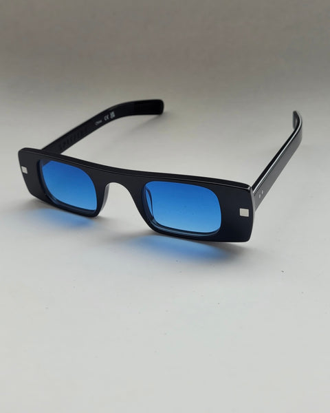 the Spitfire Cut Seven Sunglasses in black with blue lens sitting at an angle against a neutral background