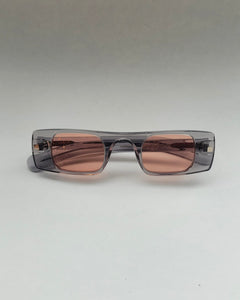 the Spitfire Cut Seven Sunglasses in grey and rose laying on a neutral background