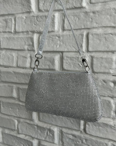 the Crystal Clutch Bag in Silver hanging against a white brick background