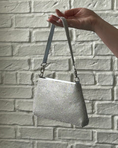 Crystal Clutch Bag in Silver held up by a hand against a white brick background