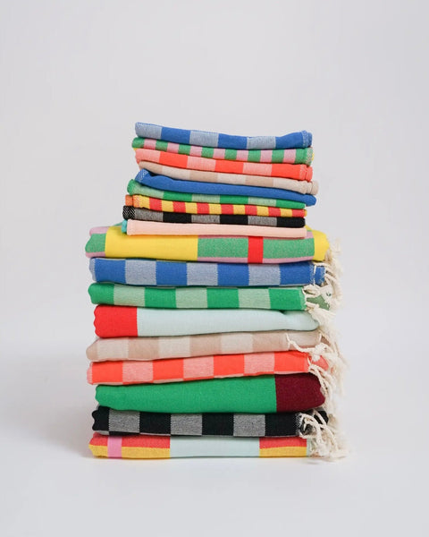 colourful striped turkish towels folded and stacked on top of one another sitting against a neutral background