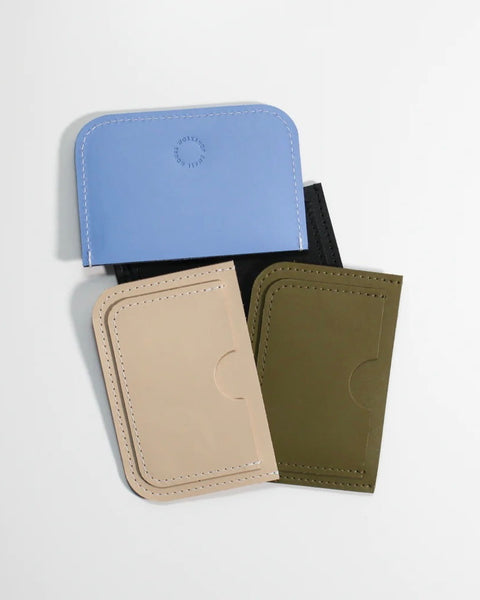 the Small Hours Leather Card Case in Sky Blue laying on top of a pile of different colour wallets against a white background
