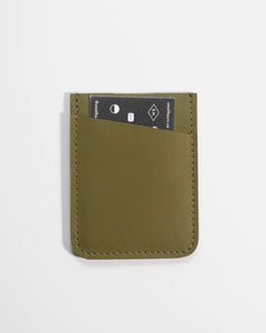 the Small Hours Slim Leather Card Holder in Olive with a card in the front pocket laying flat on a white background