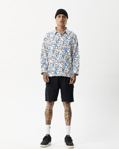 the the Afends Men's Waterfall daisy printed Long Sleeve Shirt in White on a model standing straight on staring into the camera