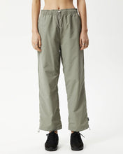 Load image into Gallery viewer, close up of the Afends Women&#39;s Octave Spray Pant in Olive on a model standing straight on with her hands by her sides

