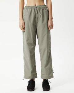 close up of the Afends Women's Octave Spray Pant in Olive on a model standing straight on with her hands by her sides