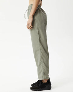 side view of the Afends Women's Octave Spray Pant in Olive on a model standing with her hands by her sides