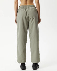 back view of the Afends Women's Octave Spray Pant in Olive on a model standing with her hands by her sides