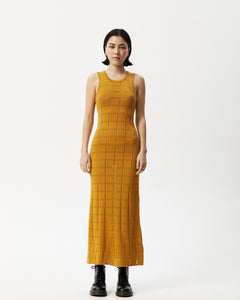 the Afends Women's Femme Dress in Mustard on a model standing straight on staring into the camera