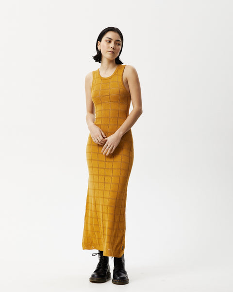 the Afends Women's Femme Dress in Mustard on a model posing with her hands in front of her body