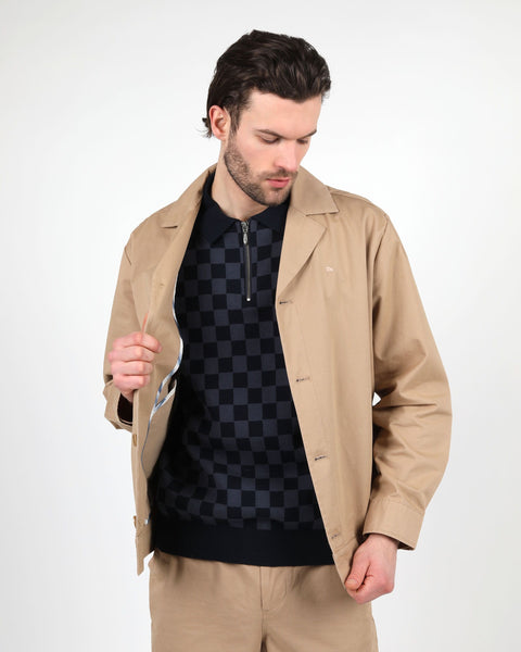 the Wemoto Men's Ethan Jacket in Khaki on a model posing with his hand on the button placket looking down and to his left
