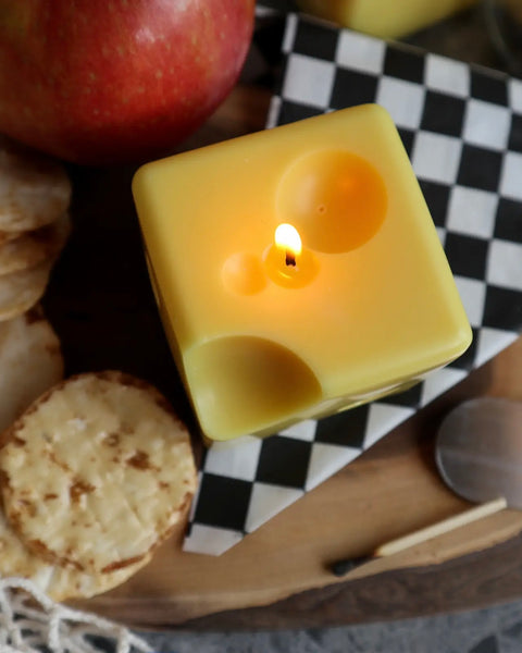 overhead shot of the Drop Dead Swiss Cheese Cube Candle lit up on a charcuterie board