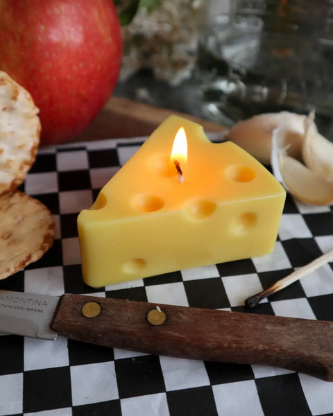 Drop Dead Swiss Cheese Slice Candle lit on a charcuterie board