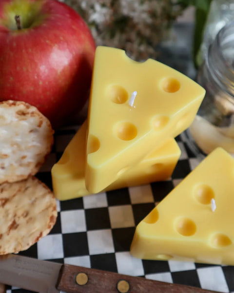 three Drop Dead Swiss Cheese Slice Candles on a charcuterie board