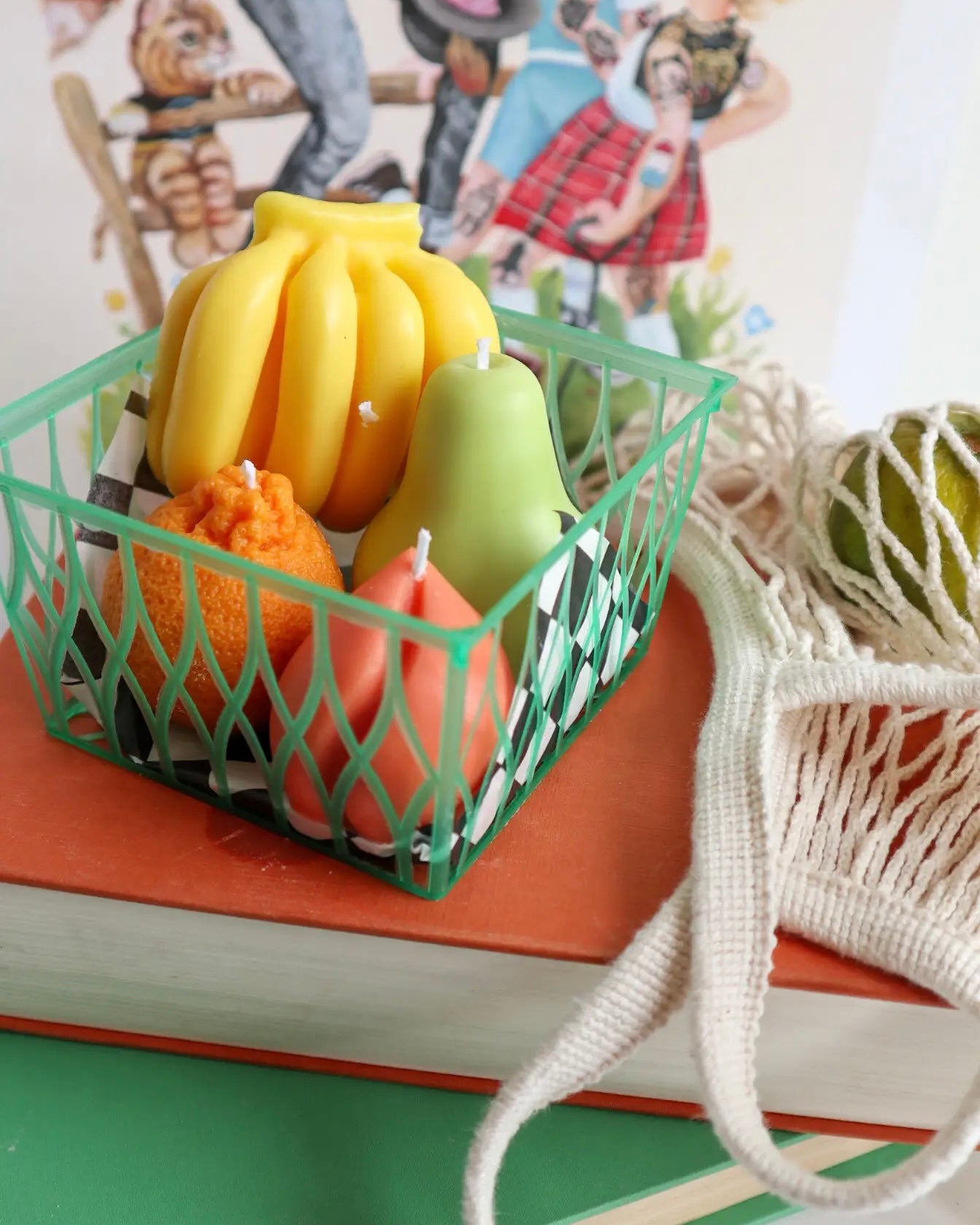 the Drop Dead Fruit Basket Candles sitting on a stack of books beside a net bag