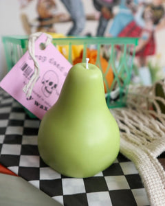 the Drop Dead pear candle sitting on a stack of books beside a net bag