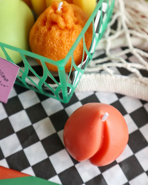 the Drop Dead peach candle sitting on a stack of books beside a net bag