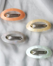 Load image into Gallery viewer, four oval hair clips in different colours shot from above laying on grey fabric
