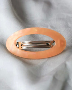 the Horace Maria oval Hair Clip in tangerine shot from above laying on grey fabric