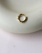 Load image into Gallery viewer, the Horace Hammered Ear Cuff in gold laying flat on a dish
