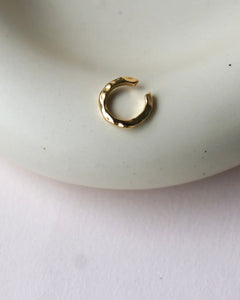 the Horace Hammered Ear Cuff in gold laying flat on a dish