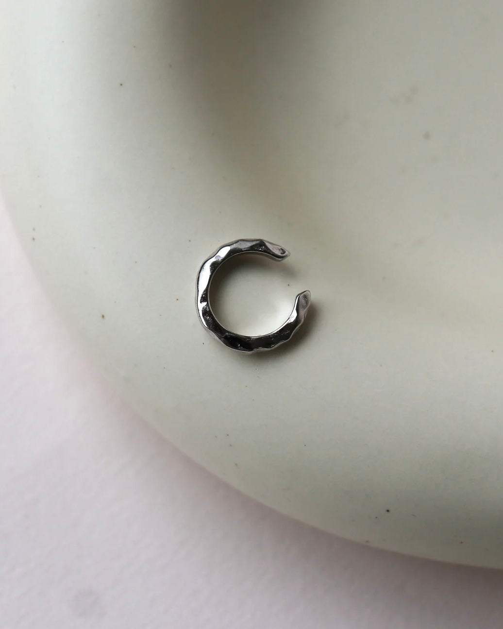 the Horace Hammered Ear Cuff in silver laying flat on a dish