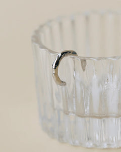 the Horace Hammered Ear Cuff in silver hanging off the side of a fluted glass dish