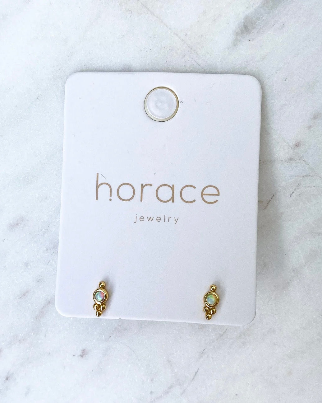 the Horace Gemma Stud Earring in gold on a branded card laying on a marble surface