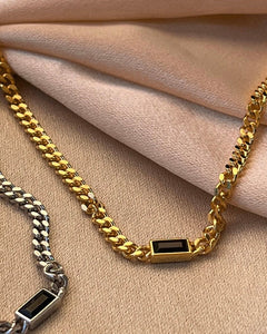 a close up shot of the Horace Nero Necklace in gold and in silver laying flat on folded pieces of fabric