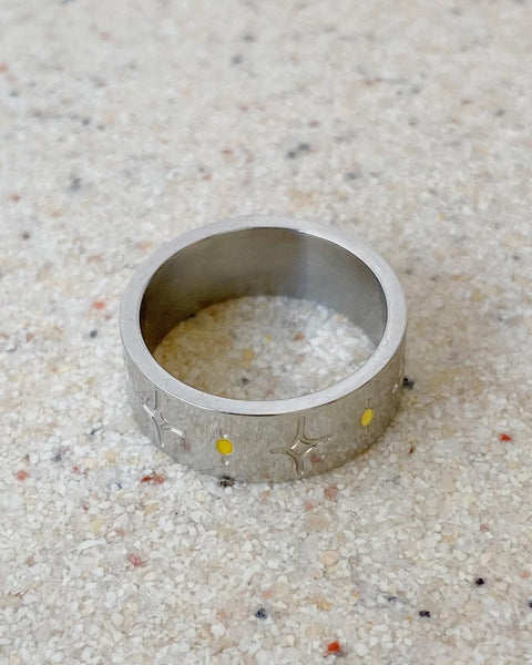 the Horace Sparka Ring in silver laying flat on a speckled stone surface