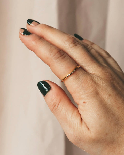 the Horace Wavy Ring in gold shown on the pointer finger of a hand with dark green nail polish