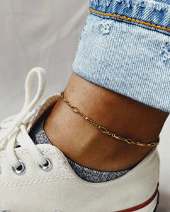 close up of the Horace Zolko Ankle Chain in gold worn by a model wearing white converse and cuffed jeans