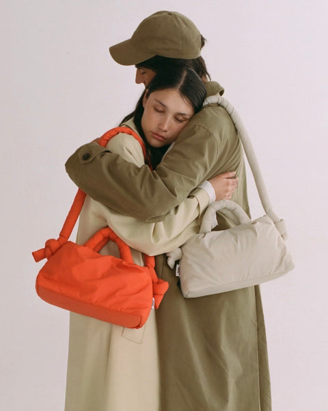 two people hugging both wearing trench coats and the Ölend Mini Ona Soft Bag standing against a neutral background