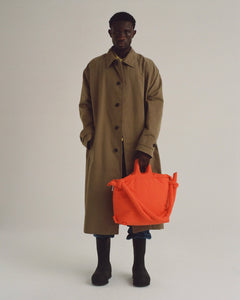 a model wearing a trenchcoat posing with the Ölend Ona Soft Bag in coral in his left hand and his right hand in his pocket