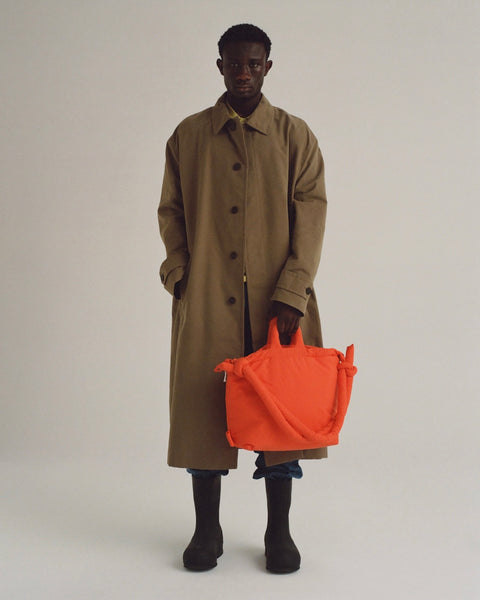 a model wearing a trenchcoat posing with the Ölend Ona Soft Bag in coral in his left hand and his right hand in his pocket