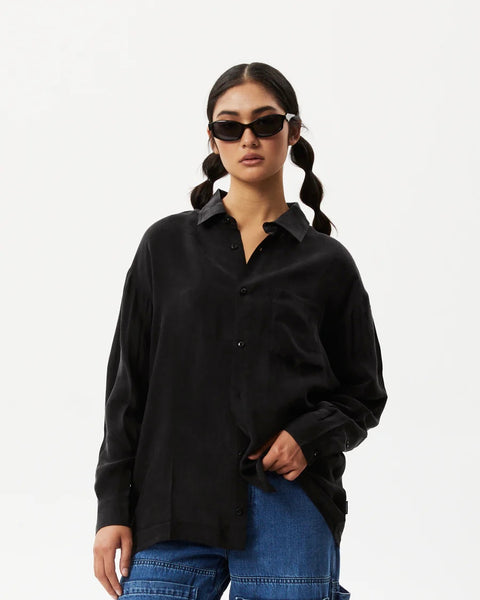 the Afends Women's Gemma Shirt in Black on a model posing with her hand in her pocket looking straight into the camera