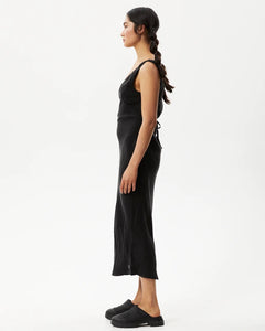 side view of the Afends Women's Gemma Dress in Black on a model posing in front of a white background
