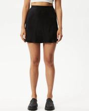 Load image into Gallery viewer, close up of the Afends Women&#39;s Gemma Skirt in Black on a model posing in front of a white background
