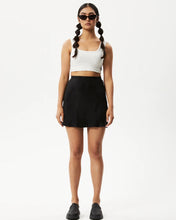 Load image into Gallery viewer, the Afends Women&#39;s Gemma Skirt in Black on a model posing in front of a white background standing straight looking into the camera
