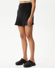 Load image into Gallery viewer, side angle view of the Afends Women&#39;s Gemma Skirt in Black on a model posing in front of a white background
