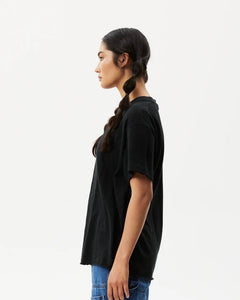 side view of the the Afends Women's Slay Oversized Tee in Black on a model posing against a white background
